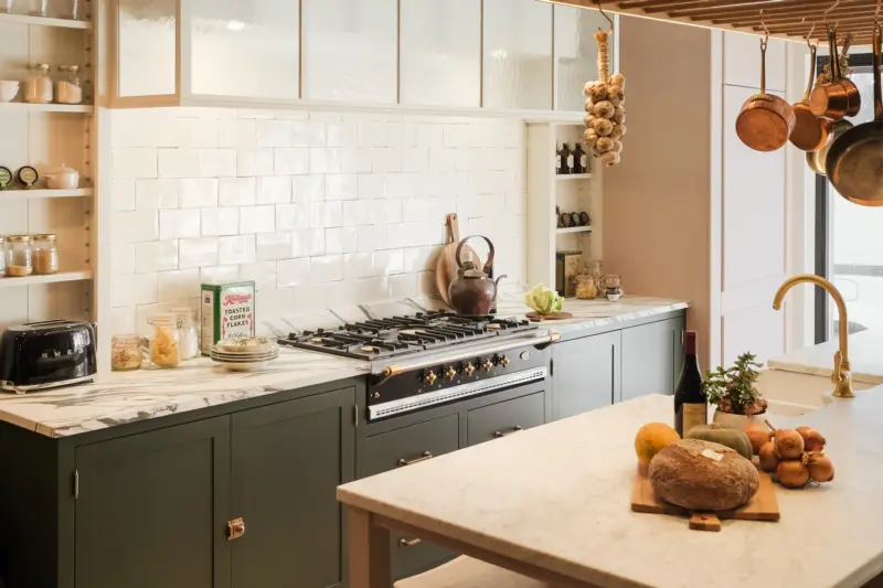 A black Lacanche range cooker with brass knobs in a kitchen with dark green cabinets and marble worktops