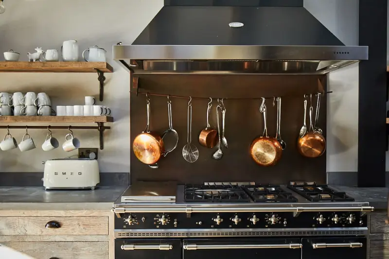 A black Lacanche range cooker with copper pans hanging above it