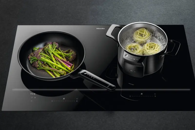 A Miele induction hob with a frying pan and a pan of pasta